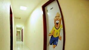 A hallway with a door featuring a cartoon character in a sports uniform. - Flats Gol de Placa (Fortaleza)