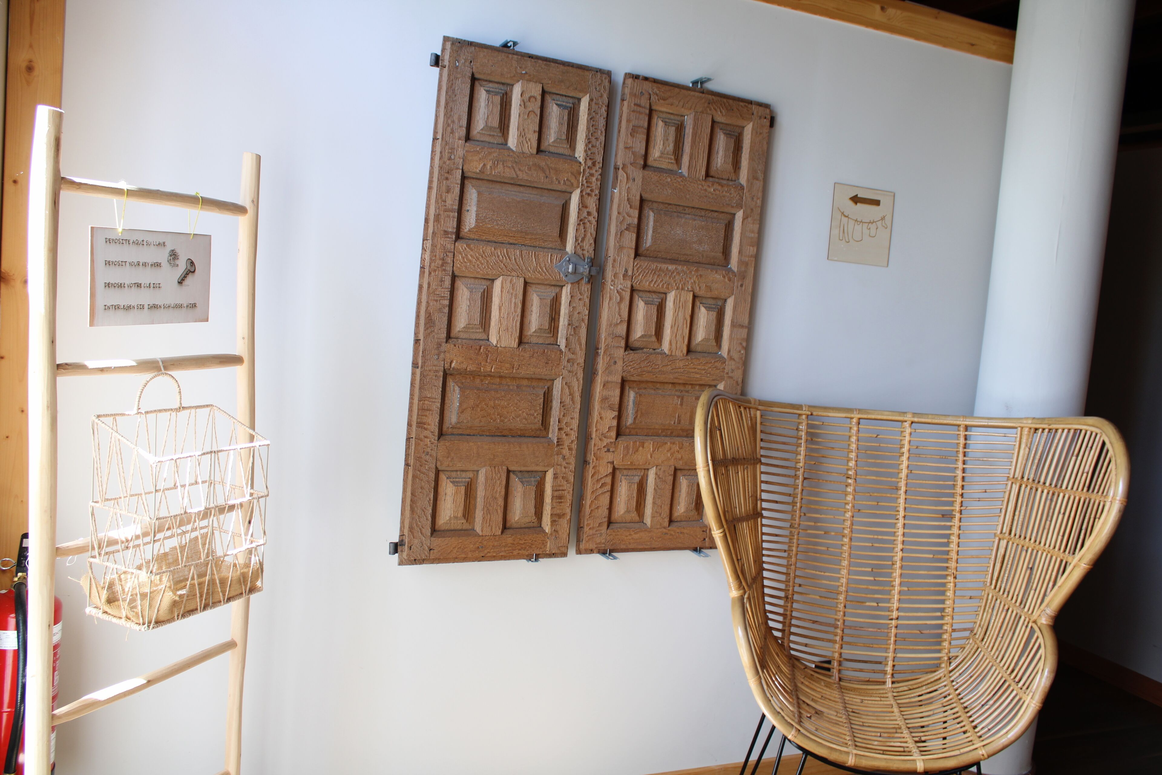 A room with a wooden door, a wicker chair, and a metal rack with a basket.