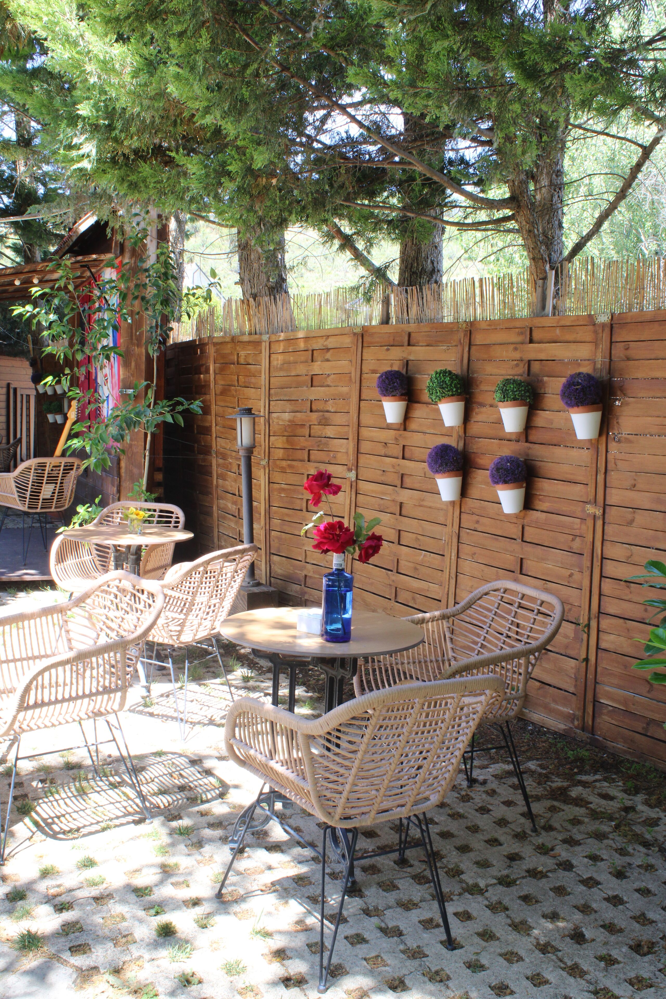Un espace patio aménagé avec des chaises en osier, une table ronde et un vase bleu orné de fleurs.