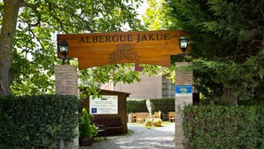 Une enseigne en bois portant le nom « Albergue Jakue » et, en dessous, une autre enseigne avec un message de bienvenue.