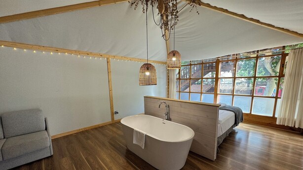 Une salle de bain moderne avec une baignoire sur pieds, un plancher en bois et une grande fenêtre donnant sur l’extérieur.