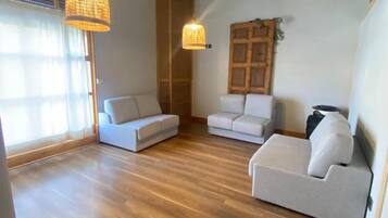 Un salon spacieux doté d’un parquet en bois, de deux canapés blancs et de deux lampes suspendues.