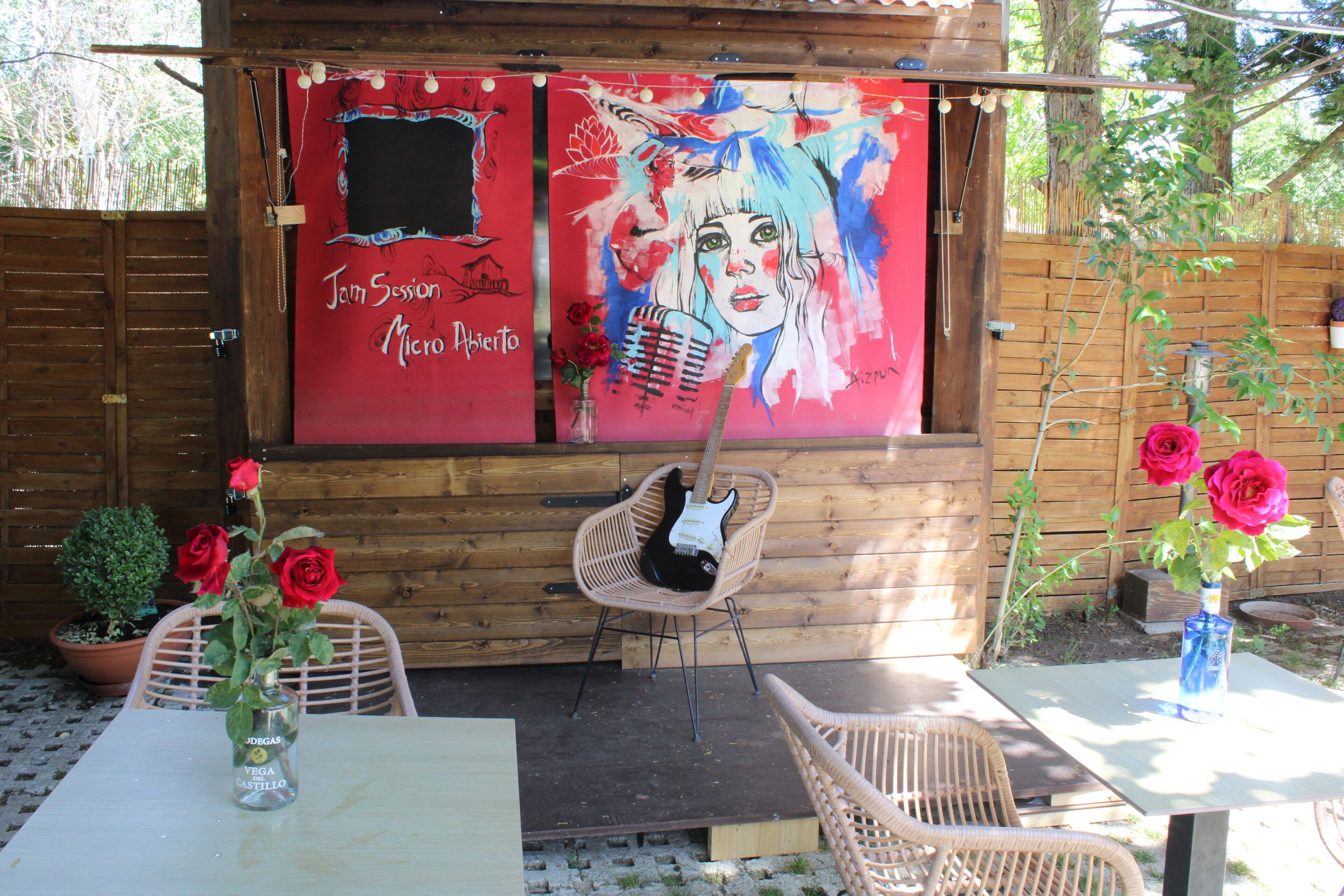 Un espacio de estar al aire libre con madera, que incluye una mesa, sillas y una guitarra.