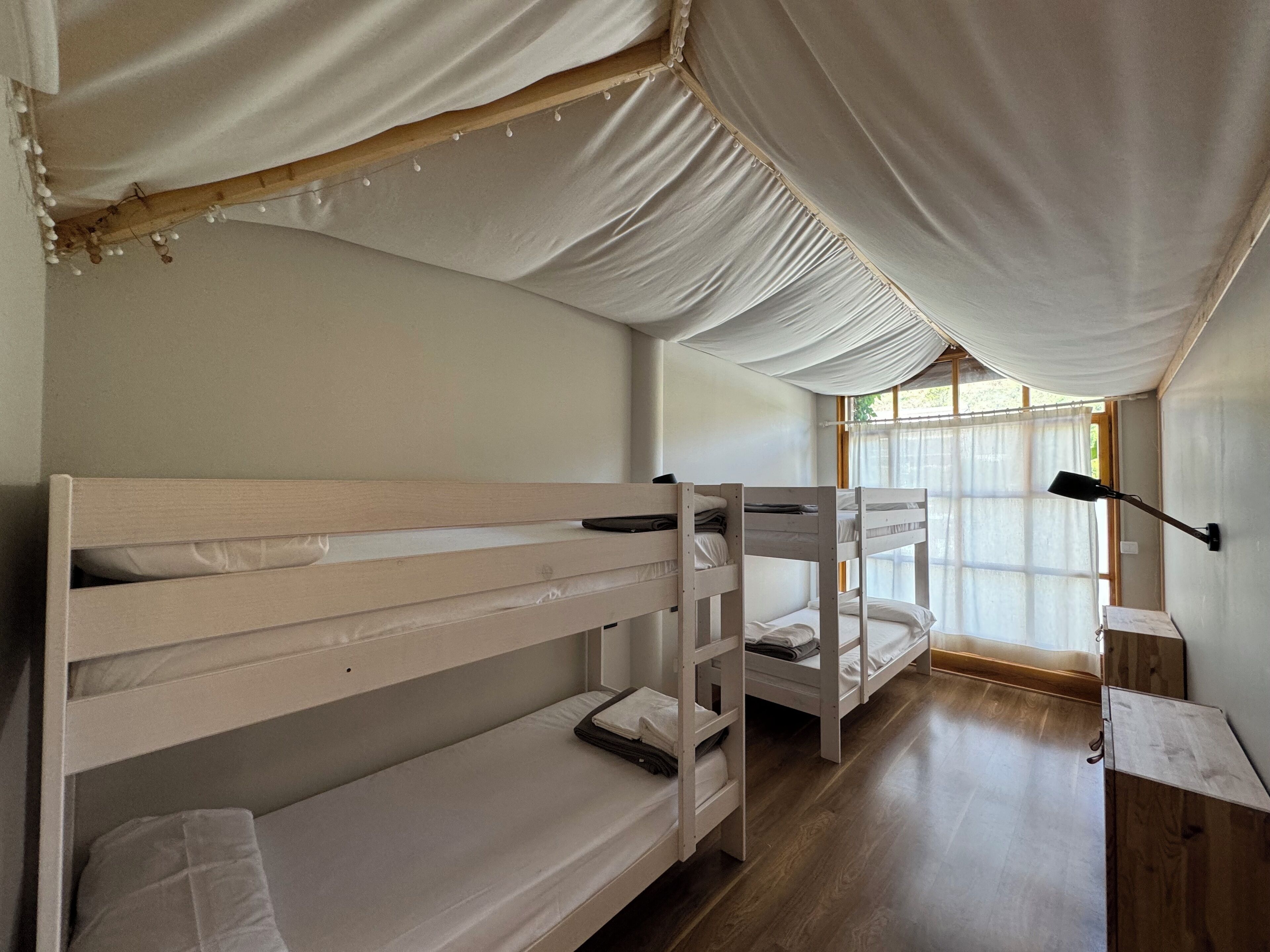 A room with bunk beds, a window with curtains, and a desk with a lamp.