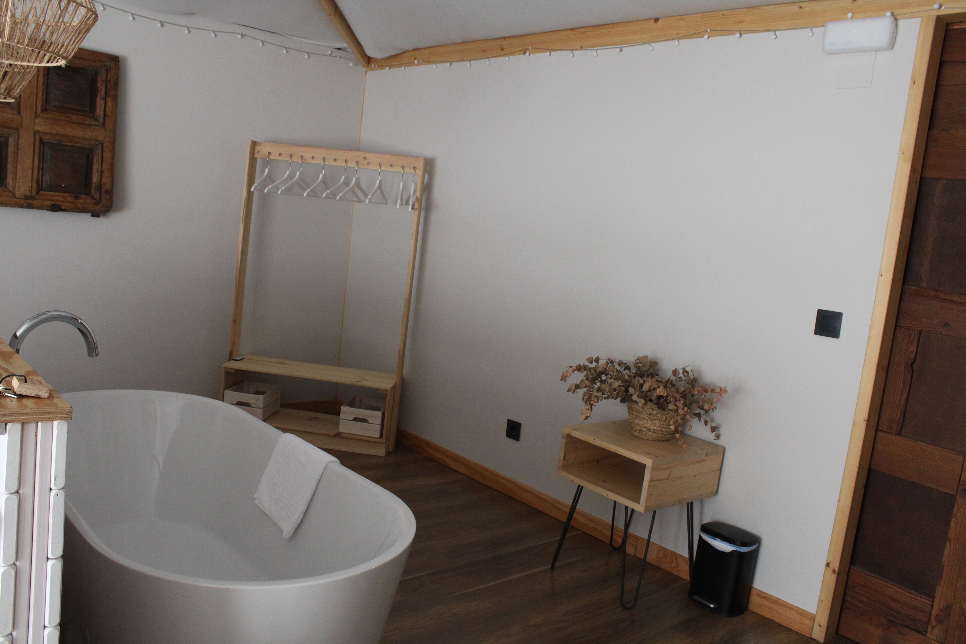 Un baño moderno con una bañera independiente, un tocador de madera, un espejo y un pequeño estante con flores secas.
