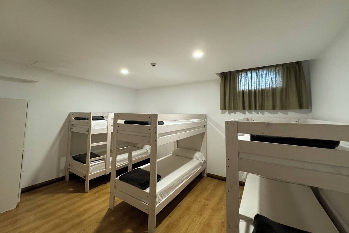 Een kamer met stapelbedden, een raam met gordijnen en een deur.