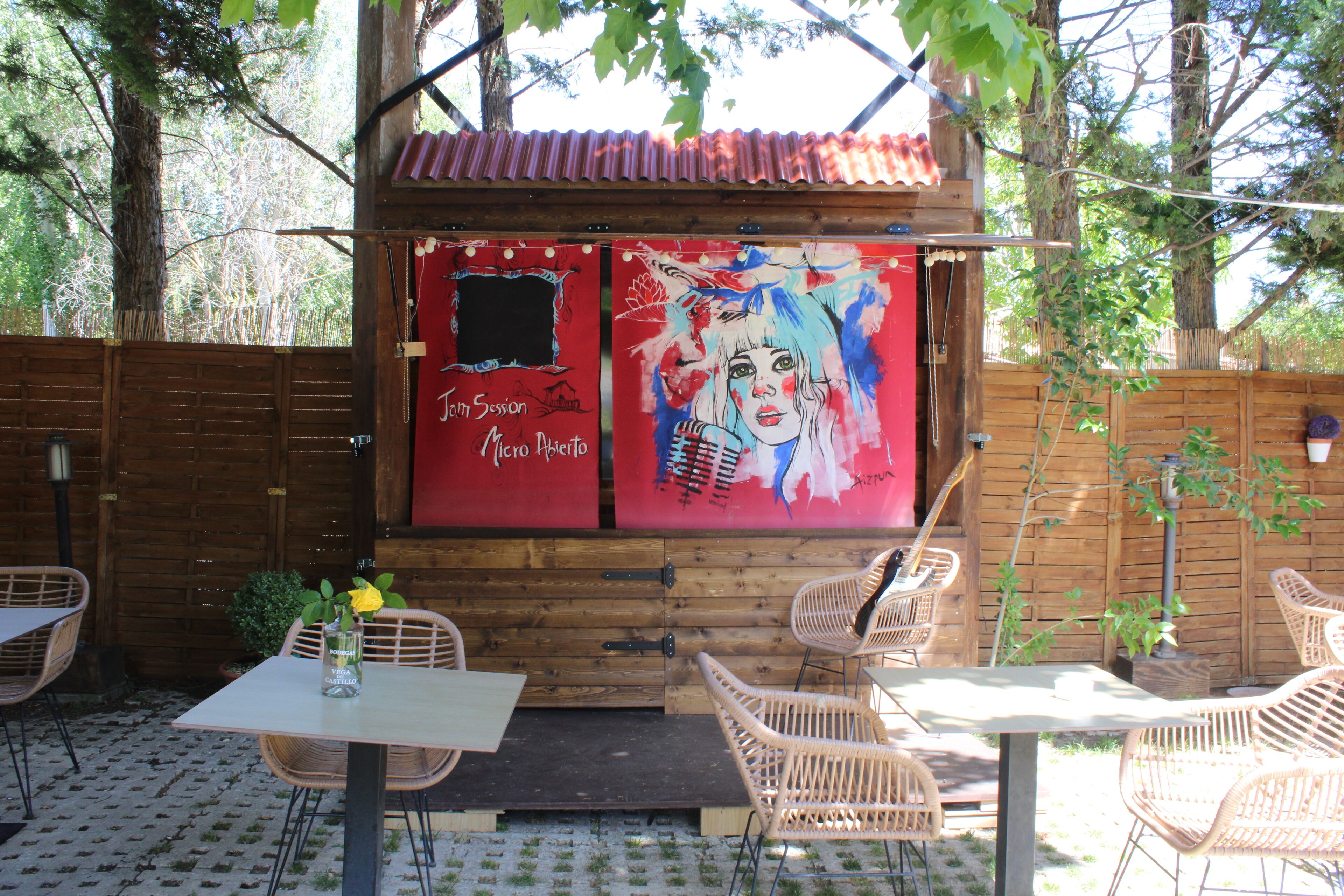 Un patio al aire libre con muebles de mimbre, una mesa con un jarrón de flores y una pared roja con grafitis.