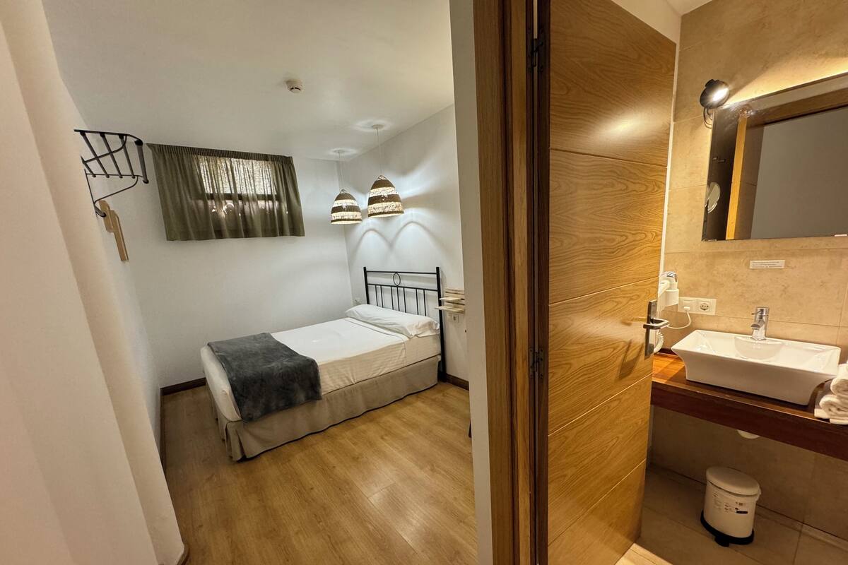 Een slaapkamer met een bed, nachtkastje en een badkamer met wastafel en spiegel.