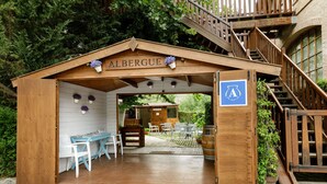 Un bâtiment en bois appelé «
ALBERGUE
», doté d’un patio couvert, d’un espace extérieur aménagé pour s’asseoir et d’un escalier menant à un étage supérieur.