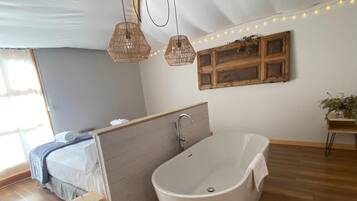 A modern bedroom with a large bed, a freestanding bathtub, and a window with curtains.