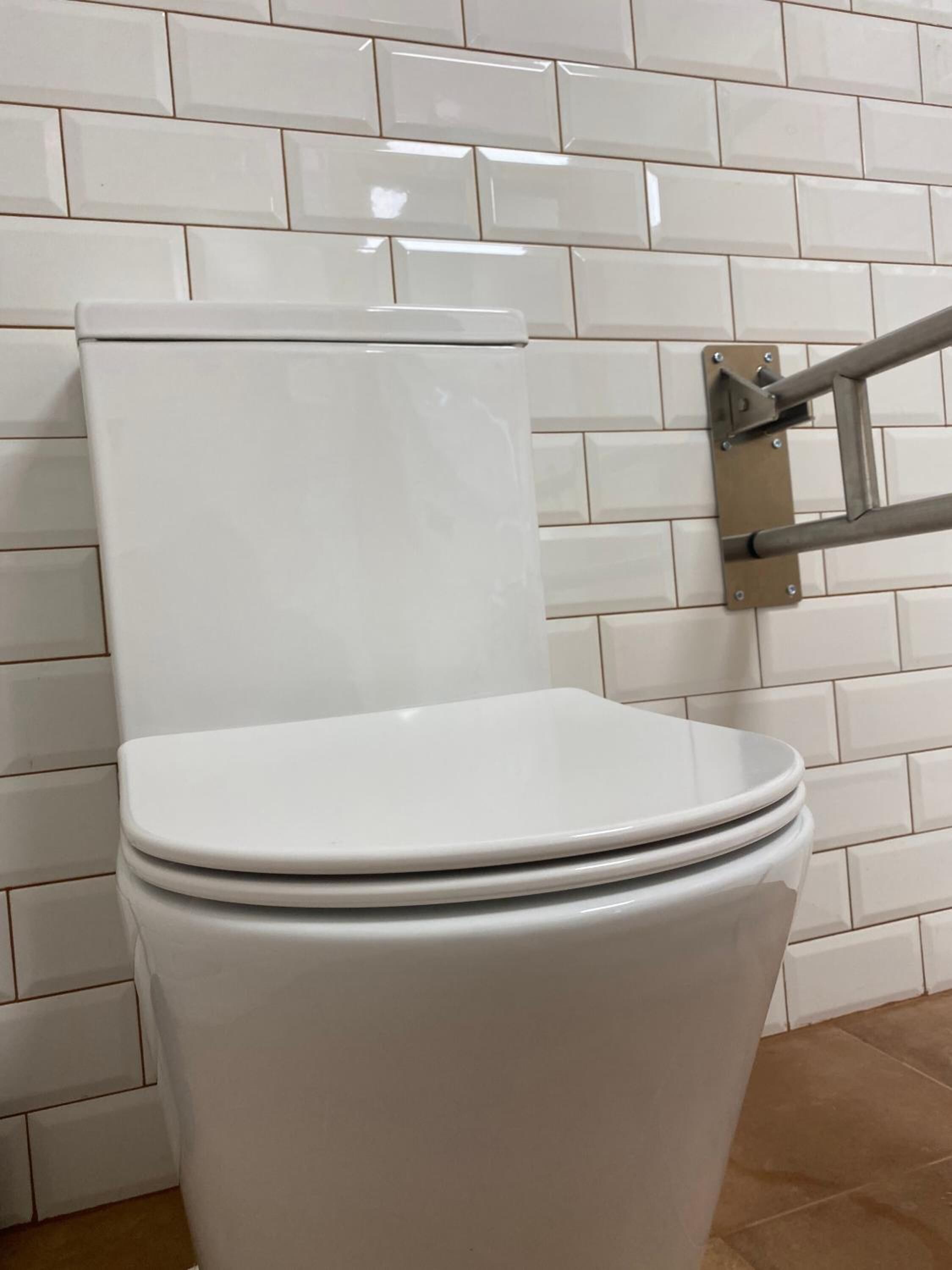 Inodoro blanco con tanque y tapa, instalado en una pared con azulejos.