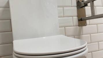 Inodoro blanco con tanque y tapa, instalado en una pared con azulejos.