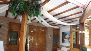 Un hall d’entrée avec des portes en bois portant les inscriptions « GLAMPING » et « ALBERQUE », des meubles en osier et une plante suspendue.
