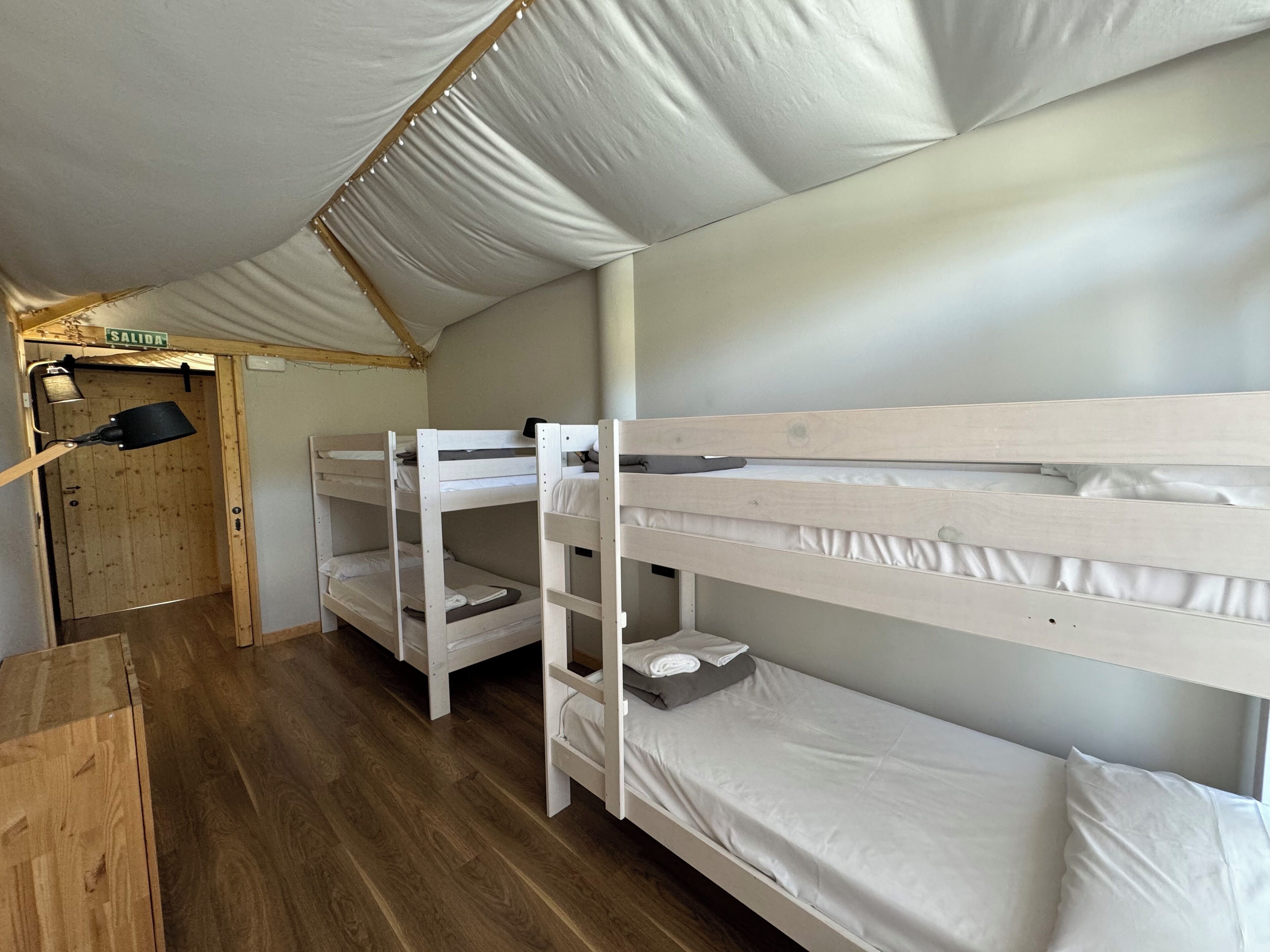 A bunk bed room with a wooden floor, a door labeled 'SALIDA', and a small table.