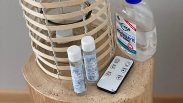 Un taburete de madera con una cesta tejida, un dispensador de gel hidroalcohólico y dos botellas pequeñas con etiquetas.