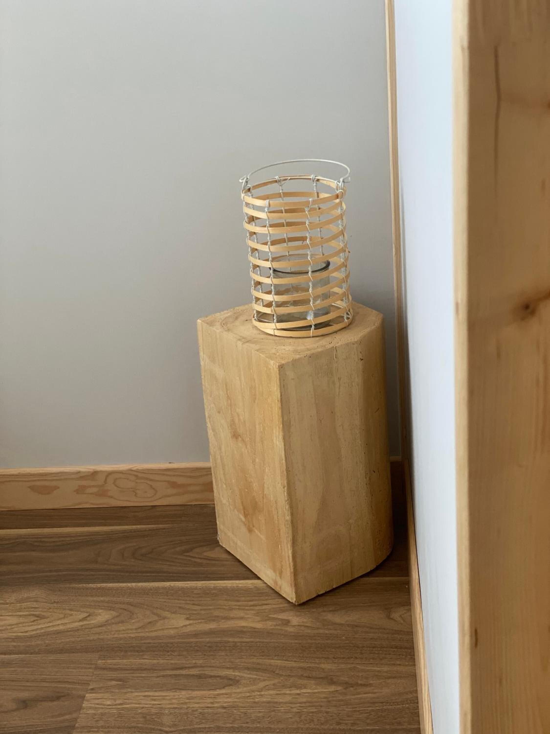 A wooden stool with a wire basket on top, placed against a wall with a wooden floor.