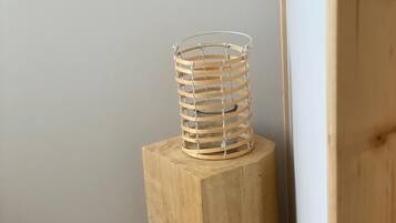 A wooden stool with a wire basket on top, placed against a wall with a wooden floor.