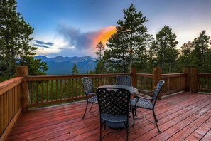 A wooden deck with a table and chairs, overlooking a mountainous landscape with a sunset. - 10 Mile Range Retreat - Peace, Seclusion & Access (Breckenridge)