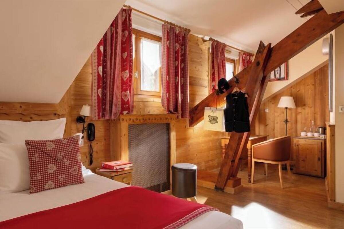 Une chambre à coucher avec un lit, une couverture rouge, une échelle en bois, un bureau et une chaise.