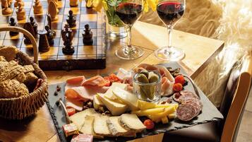 Un tablero de ajedrez, una copa de vino tinto y una tabla de fiambres con diferentes quesos y embutidos.
