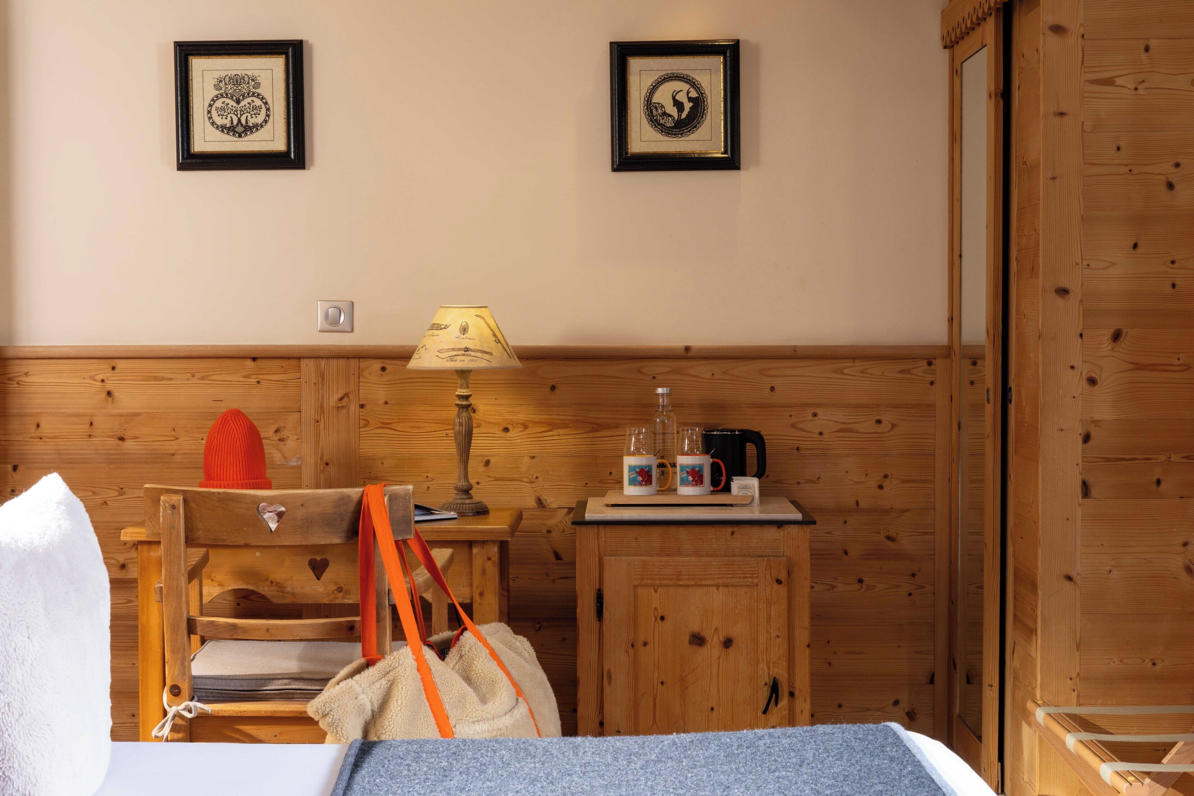 A wooden room with a bed, a small table with a lamp, a cabinet, and two framed pictures on the wall.