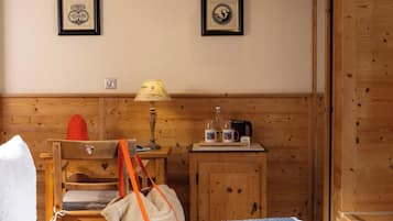 A wooden room with a bed, a small table with a lamp, a cabinet, and two framed pictures on the wall.
