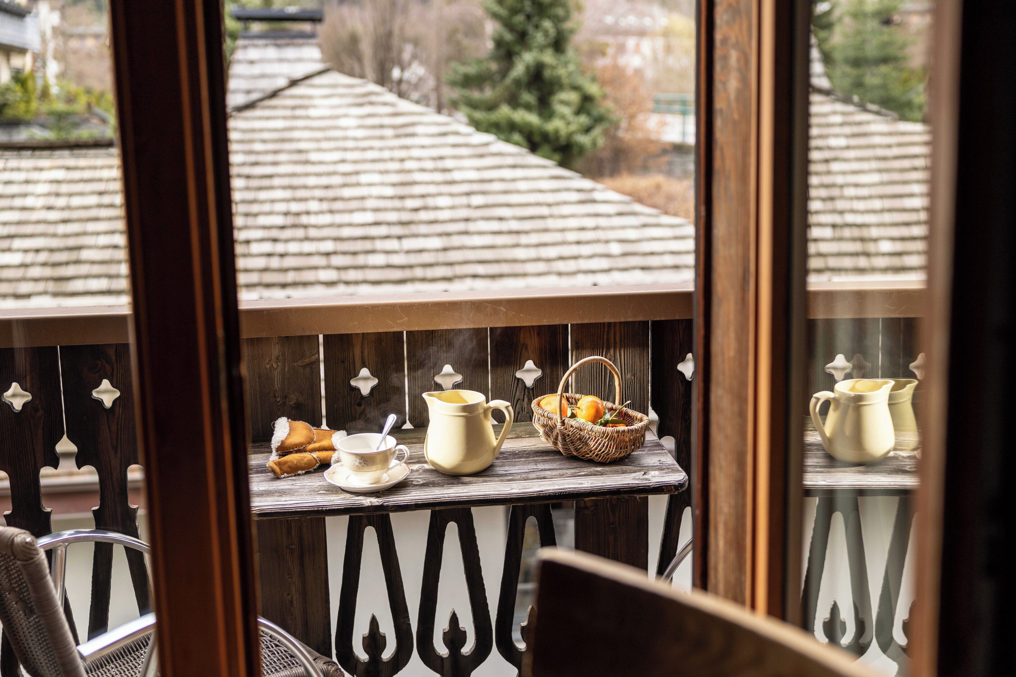 A balcony with a table set for breakfast, including a pitcher, cups, and a basket of fruit.