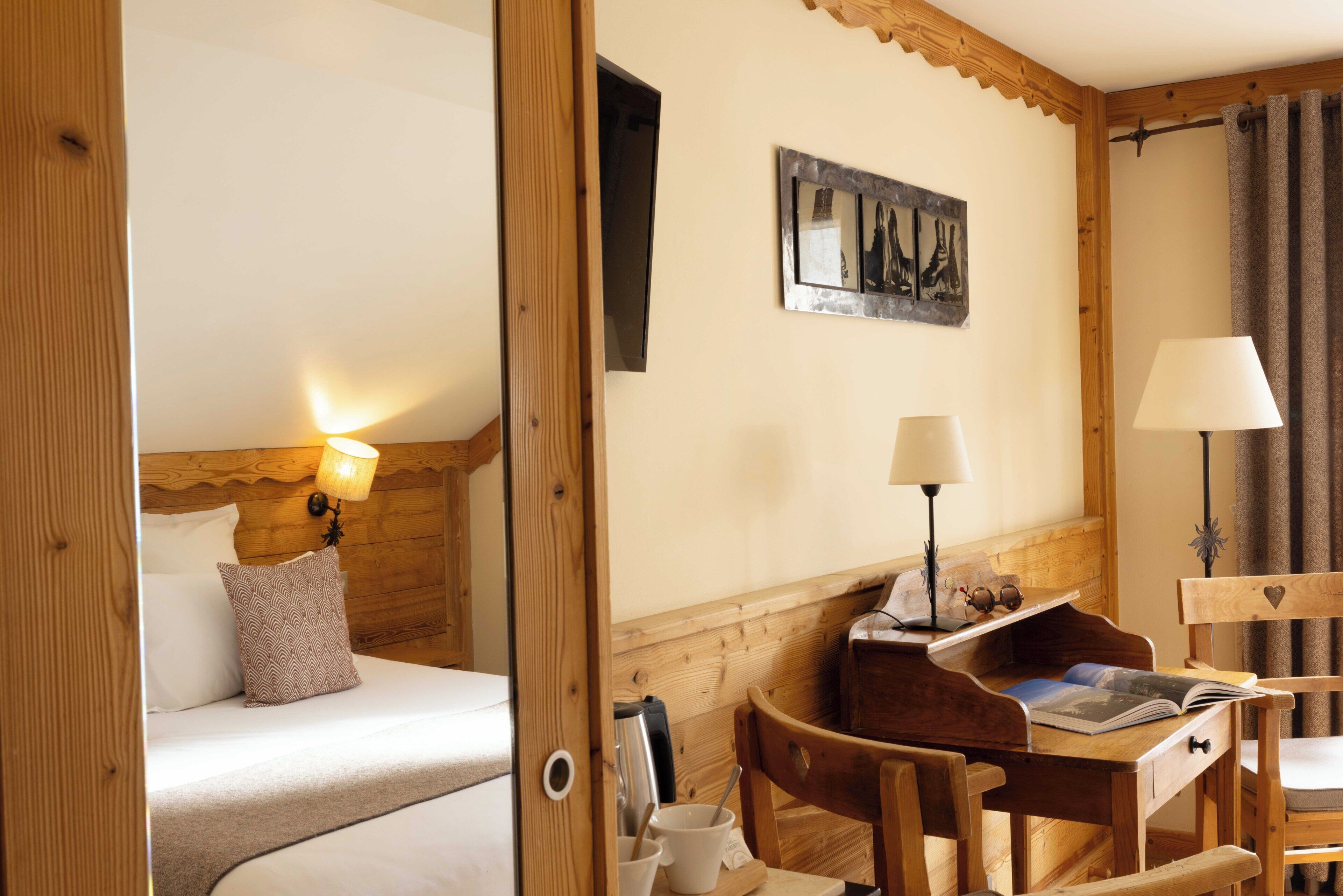 Une pièce en bois avec un lit, un bureau et une chaise. Il y a une lampe sur le bureau et un tableau au mur.