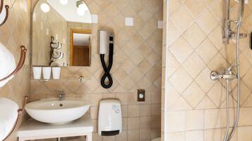 Een badkamer met een wastafel, spiegel, handdoekhouder en een douche met een handdouche.