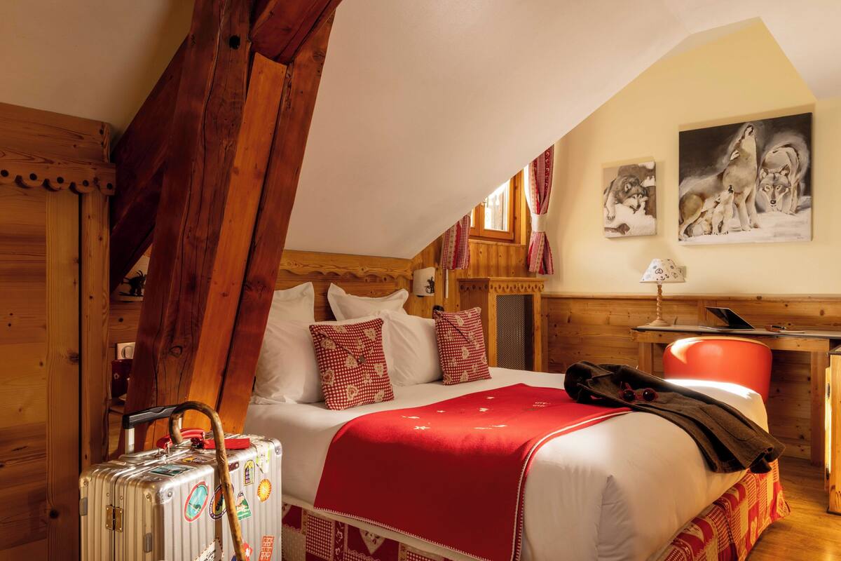 Une pièce aménagée comme un chalet en bois, avec un lit, une valise et un bureau doté d’une lampe.