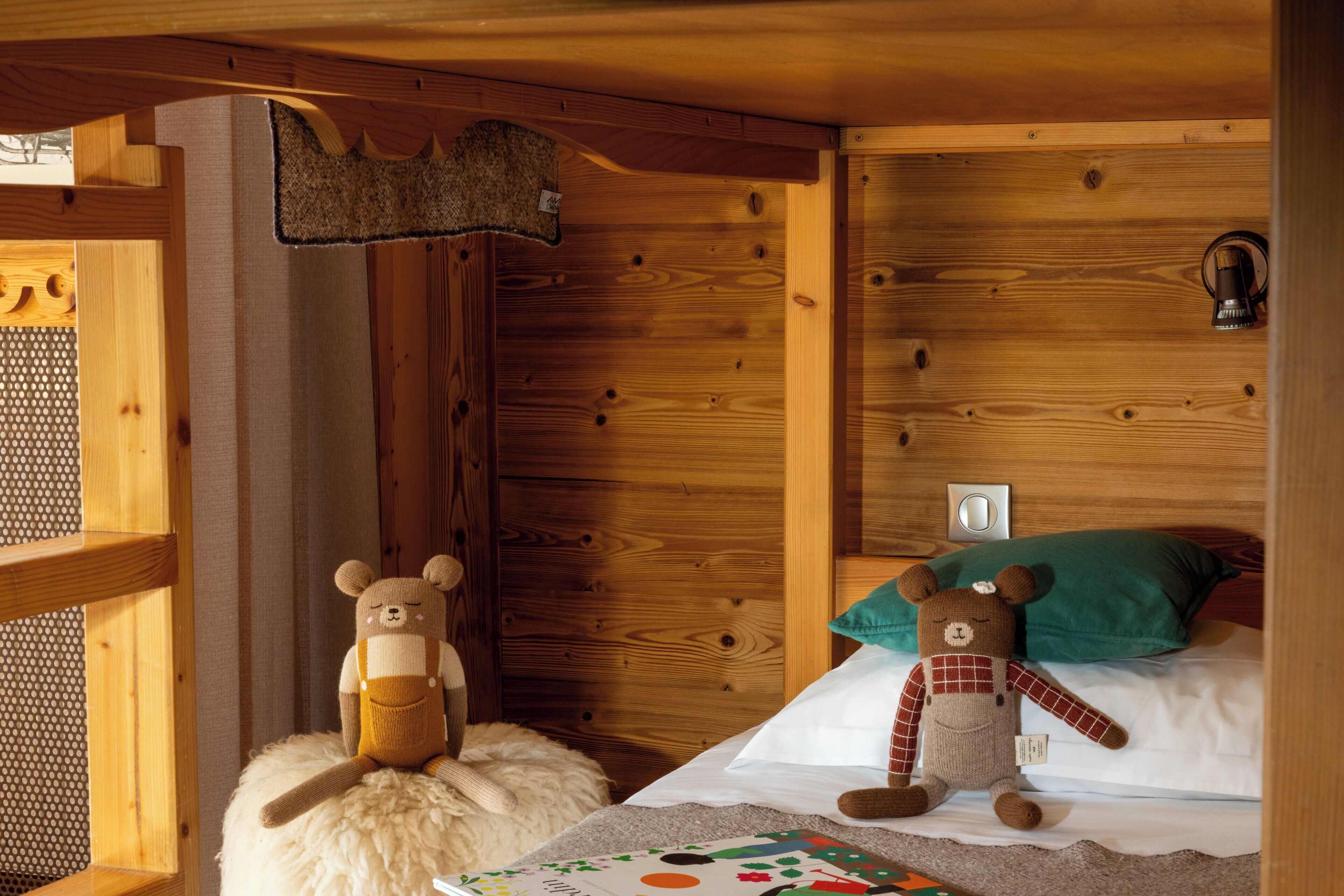 A wooden cabin interior with two plush bears on a bed, a green pillow, and a small rug.