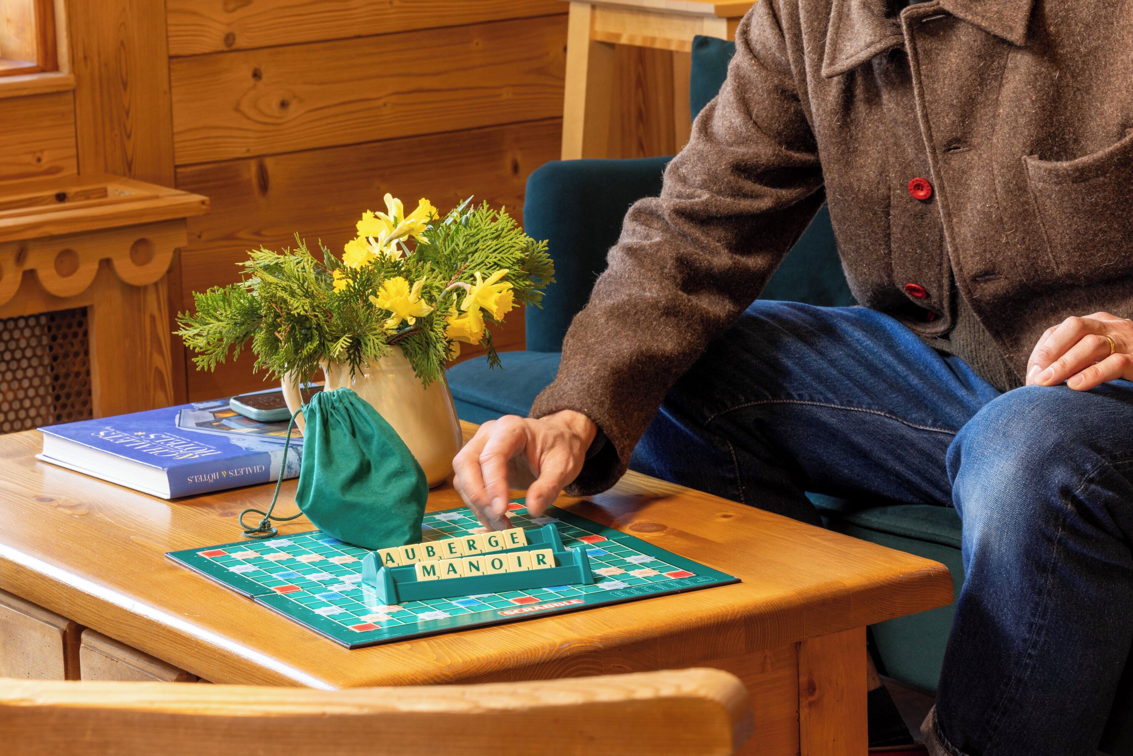 A wooden table with a board game, a book, and a vase with flowers.