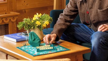 A wooden table with a board game, a book, and a vase with flowers.