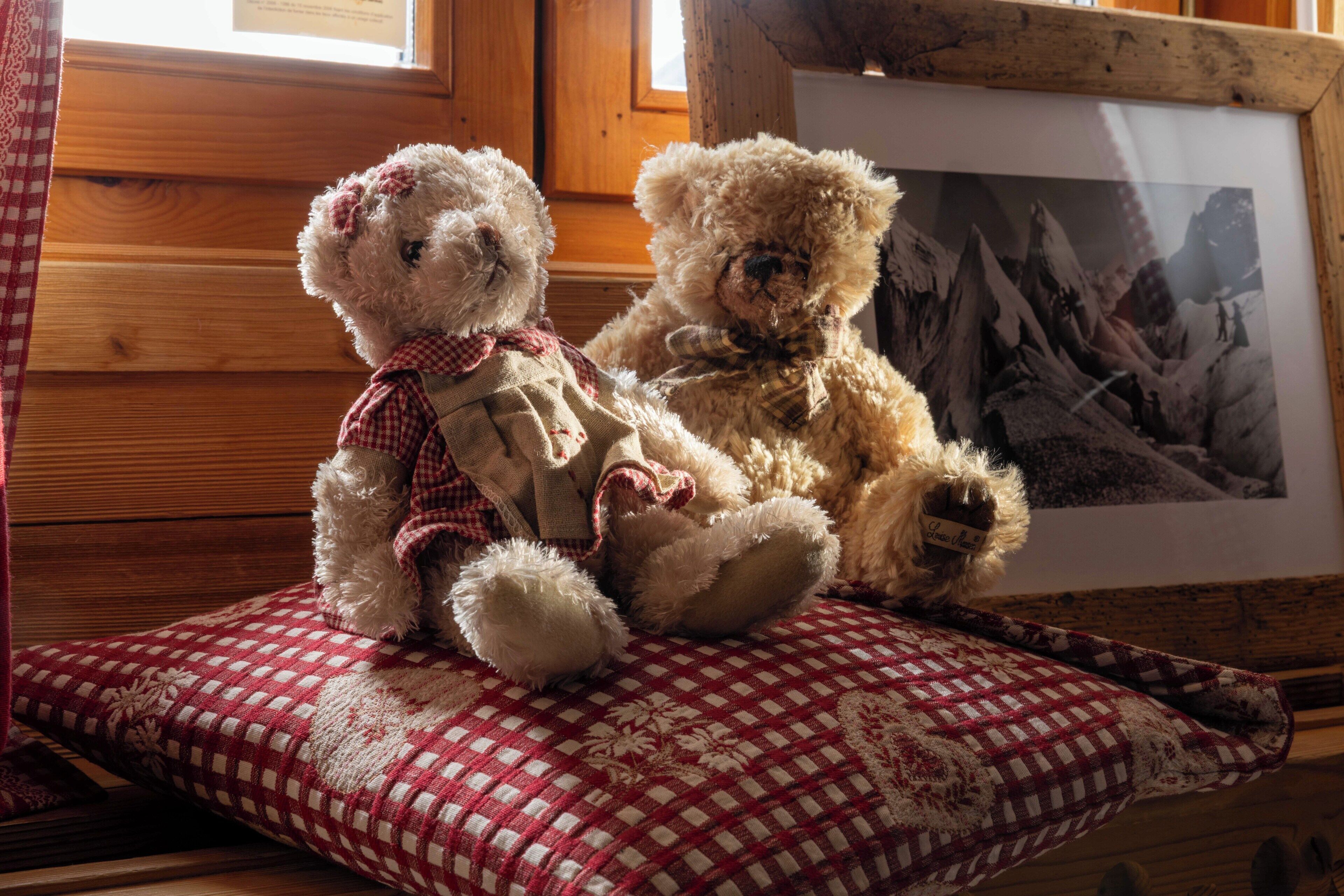 Two teddy bears on a checkered cushion with a framed picture in the background.