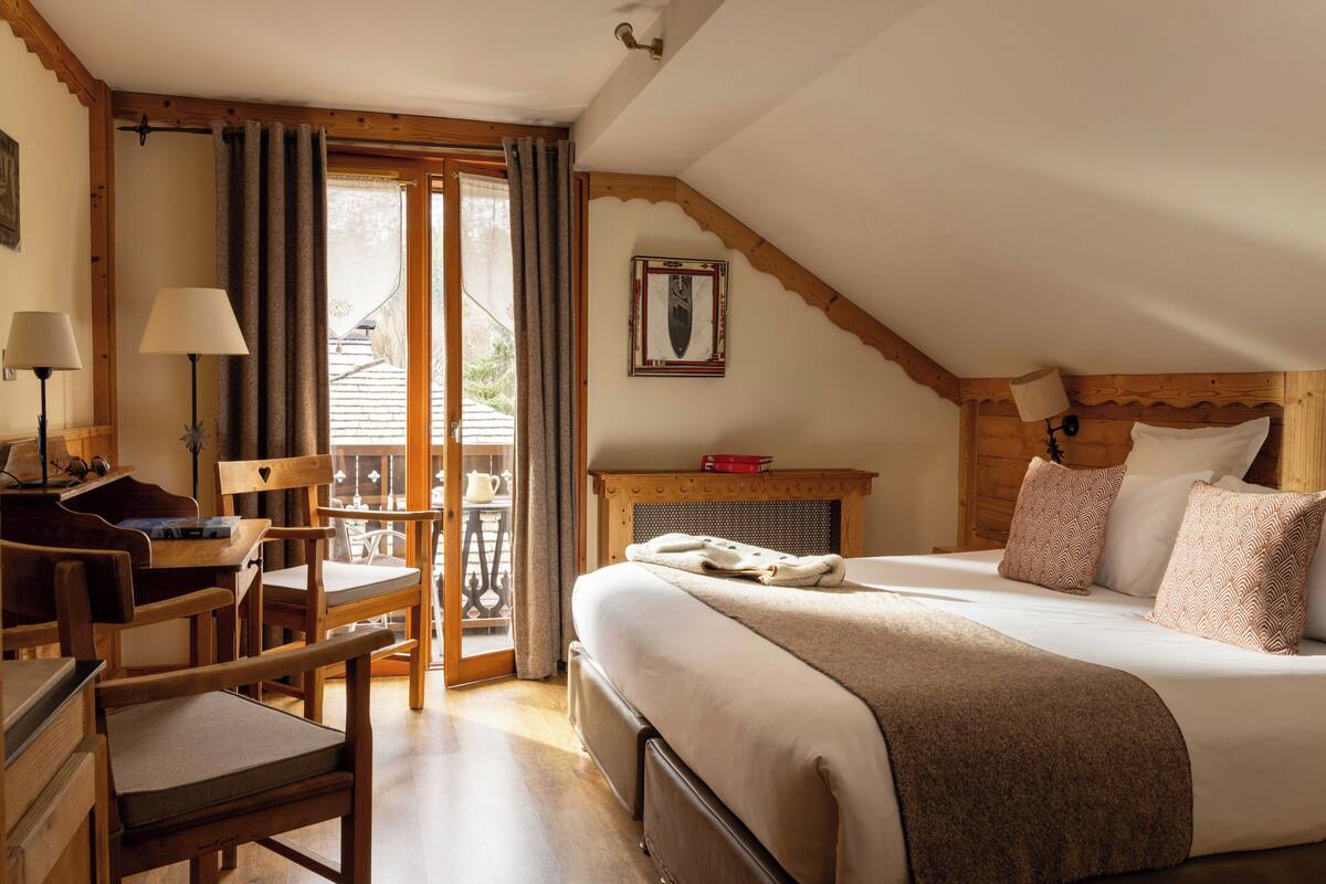 Une chambre à coucher comprenant un lit, un bureau, une chaise, une fenêtre avec des rideaux et un plafond en bois.