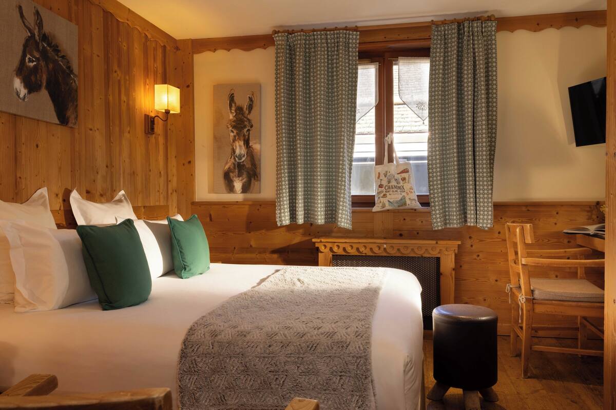 Une pièce en bois avec un lit, des oreillers, une lampe, un téléviseur fixé au mur et des rideaux.