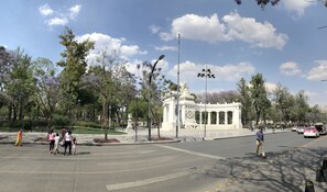 Une place publique avec un monument central, des arbres tout autour et un passage piéton.
