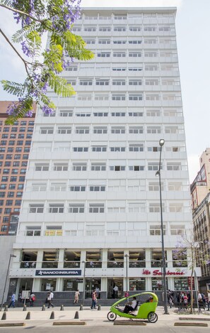 A multi-story building with a modern architectural design, featuring a large number of windows and a ground-level commercial space with visible signage for a bank and a store. - Boutique Apartment Carso Alameda 1102 (Mexico City)