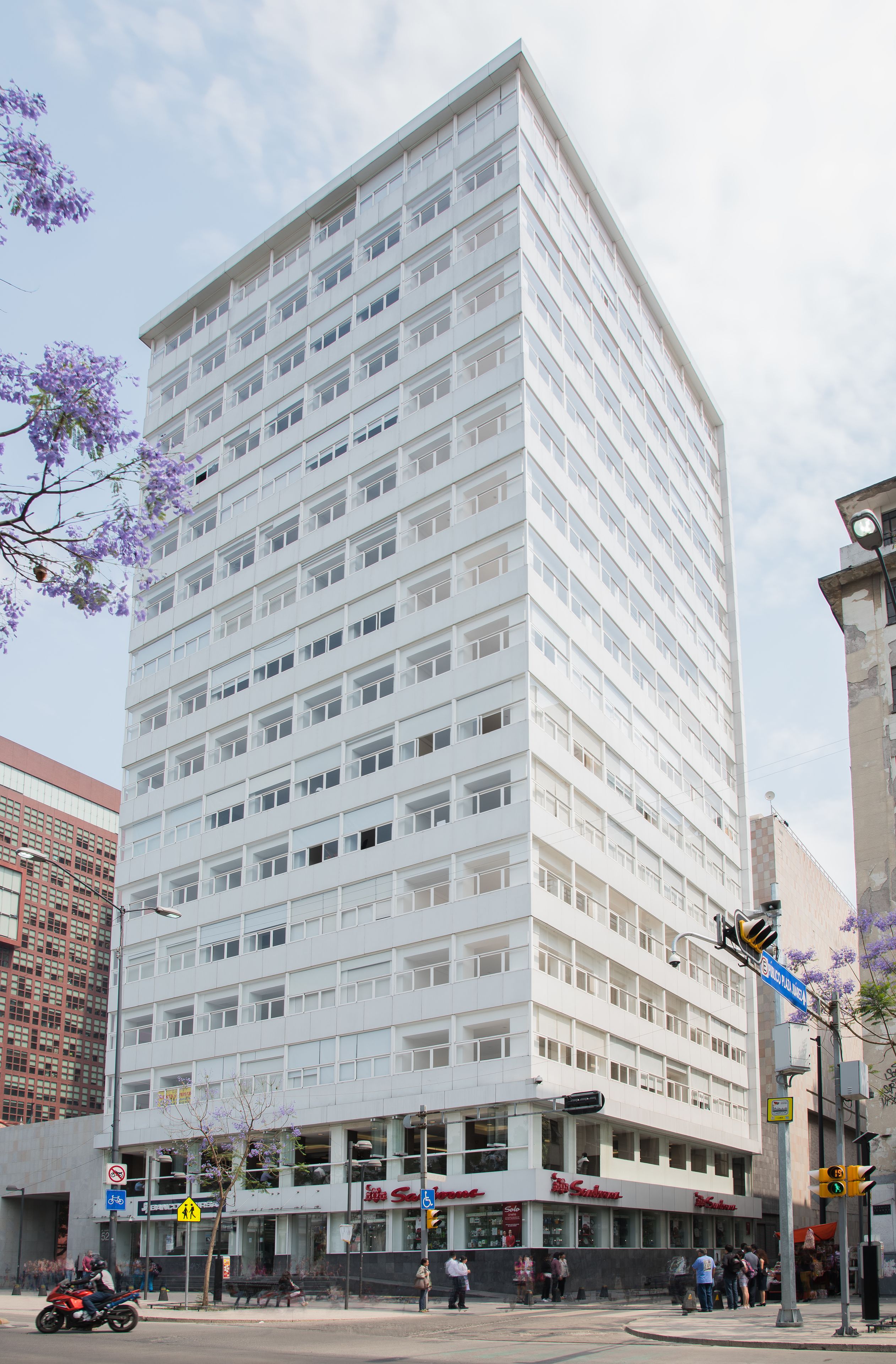 A multi-story building with a flat facade, large windows, and a ground-level commercial area with shops.
