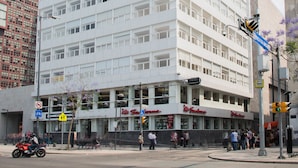 Un edificio de varios pisos con fachada plana, amplias ventanas y un área comercial en la planta baja con tiendas.