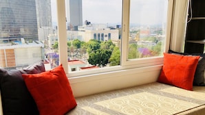 Vista de la ciudad desde una ventana con un sofá estampado y cojines rojos.