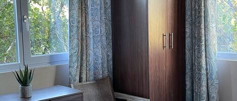 A bedroom with a bed, a desk with a plant, a chair, and a wardrobe.