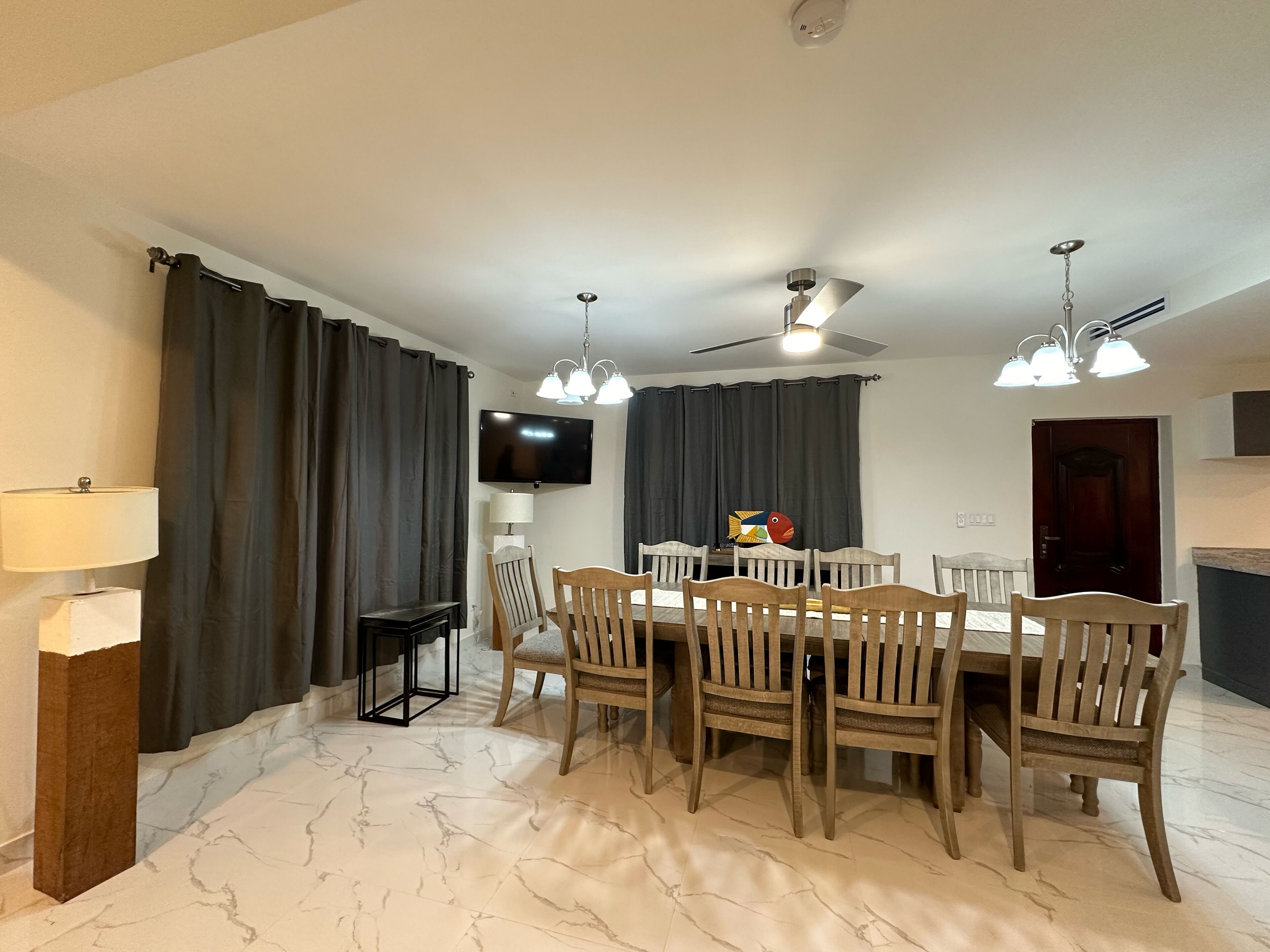 A dining area with a table and chairs, a TV mounted on the wall, and a ceiling fan.