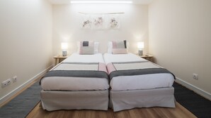 A twin room with two beds, bedside tables, wall-mounted lamps, and a hanging floral decoration. - Lis Apartments (Lisbon)