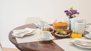 A breakfast table with a fruit plate, a muffin, a teapot, cups, and a vase of flowers. - Lis Apartments (Lisbon)