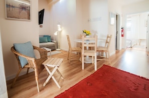 Een gezellige woonkamer met een rieten stoel, een klein houten tafeltje en een rode vloerkleed.