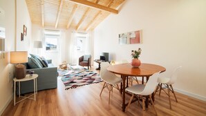 A modern living room with a wooden ceiling, a round dining table with white chairs, a grey sofa, and a colorful rug. - Lis Apartments (Lisbon)