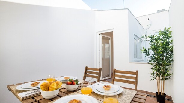A small outdoor dining area with a table set for breakfast, including pastries, fruit, and orange juice. There are two chairs and a potted plant nearby. - Lis Apartments (Lisbon)