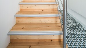 A wooden staircase with metal railings leading to a room with white walls and a patterned floor. - Lis Apartments (Lisbon)