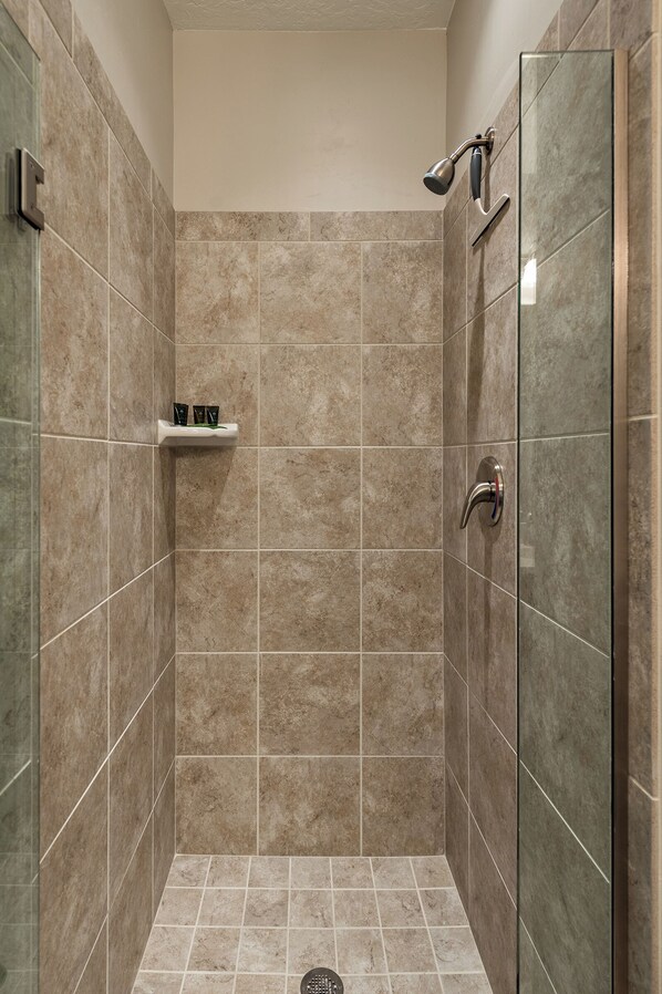 A walk-in shower with beige tiles, a glass door, and a shelf with toiletries.